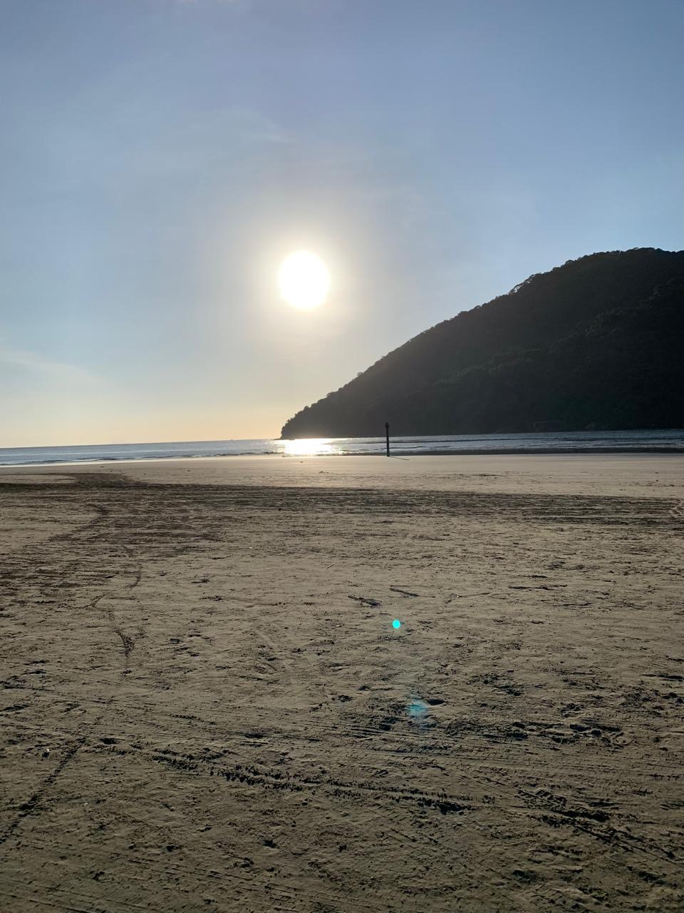 Sol sobre o mar e a faixa de areia junto ao morro